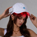 Person wearing a white Hisooth scalp massage cap with a battery attached, emitting red light.